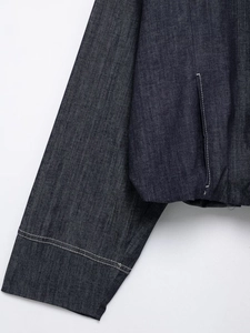 Detailed view of dark indigo denim jacket showing contrast stitching and pocket craftsmanship