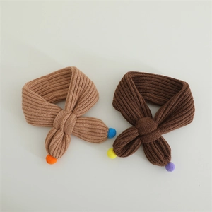 Detail of knit baby scarves in camel and brown with colorful pom-pom decorations