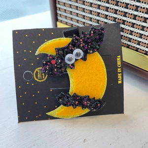 Détail de la pince à cheveux Halloween avec chauve-souris pailletée et lune jaune brillante