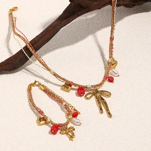 Detail of red and gold woven necklace with butterfly pendant on wooden branch