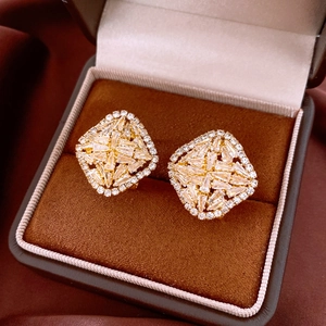 Macro shot of gold diamond-shaped earrings with zircon stones on brown velvet padding