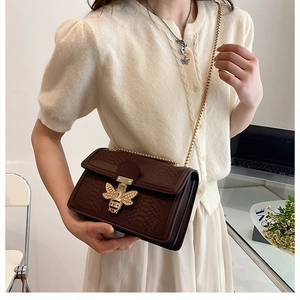 Detail of dark brown croc-embossed leather bag with gold bee buckle and pearl accents