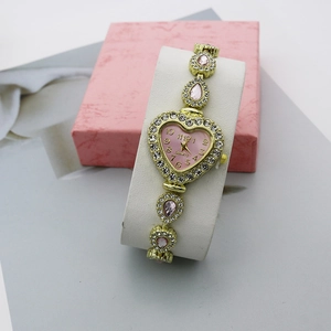 Gros plan d'une montre à quartz cœur rose avec bracelet doré et strass brillants