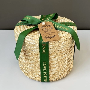 Detail view of a round woven straw gift box featuring a green ribbon and pearl accent