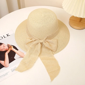 Close-up of beige paper straw hat with large bow detail on a minimalist desk