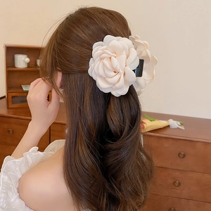 Close-up of a large cream fabric camellia flower hair claw clip on a woman's bun
