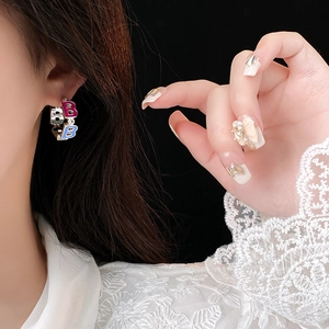 Close-up of elegant letter earrings in blue and rose red enamel on a female model
