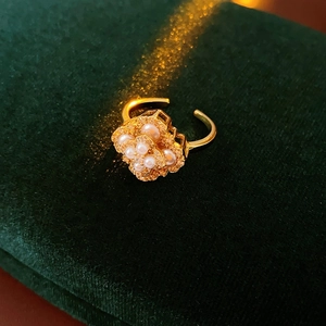 Détail macro d'une bague trèfle dorée avec perles et cristaux sur velours vert
