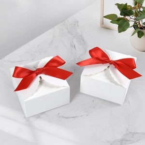 Detail of white square gift boxes with red satin bows on marble surface backdrop