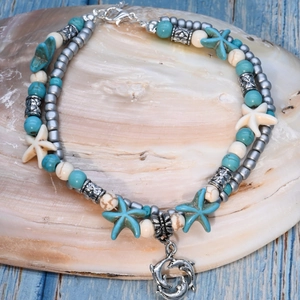 Detail of beaded beach anklet with turquoise stones and silver dolphin pendant on shell