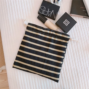 Detailed view of a striped linen drawstring pouch with cosmetics on a quilted surface
