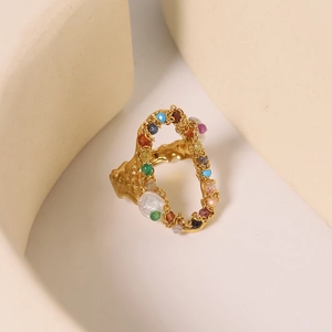 Minimalist gold titanium steel ring with colorful gems and pearl on a beige surface