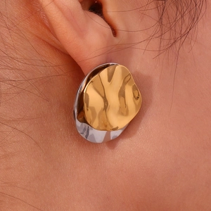Close-up of gold and silver layered irregular stud earrings with pleated metal texture