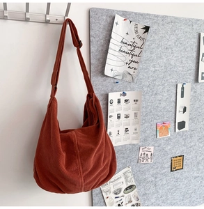 Detail view of brick red corduroy hobo bag hanging on wall with adjustable shoulder strap