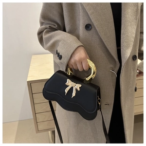 Detail of matte black crossbody bag with golden bow buckle and curved wavy bottom