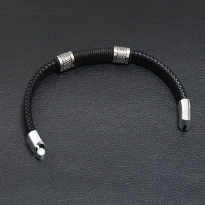 Close-up of black braided leather bracelet featuring three textured silver metal charms