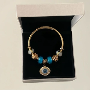 Detailed close-up of golden evil eye charm bracelet with blue beads in a gift box