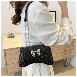 Close-up of black sequined chain bag featuring a silver bow decoration and curved design