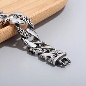 Macro view of silver stainless steel Cuban chain bracelet with Greek key engraving patterns