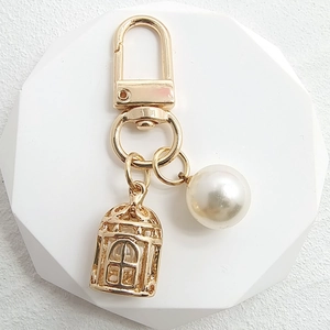 Detail of a golden birdcage keychain with a white pearl charm on a geometric base