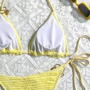 Detailed flat lay of light yellow bikini with gold butterfly accents and lace backdrop