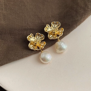 Macro shot of gold floral earrings with natural baroque pearls on a textured background
