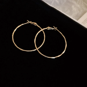 Detailed view of large gold circular earrings featuring a hammered metal texture finish