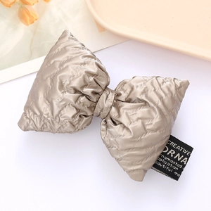 Champagne padded faux leather bow hair accessory with elegant quilted texture on white tray