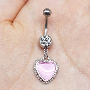 Detailed macro view of a silver belly ring with a pink heart pendant held in a hand