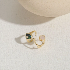 Detail of two gold open rings featuring abalone shell and pink zircon on stone surface