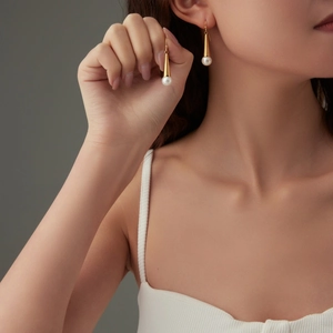 Elegant gold tapered metal and white round pearl drop earrings worn by a model