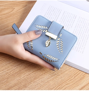 Detail of light blue short wallet with leaf cutout design and gold leaf pendant in hand
