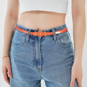 Orange skinny belt with three floral buckle decorations worn on denim jeans