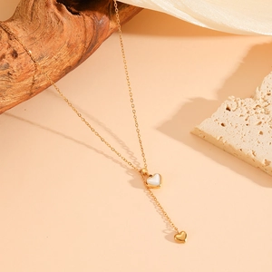 Detail of 18k gold plated double heart necklace with white shell inlay on stone backdrop