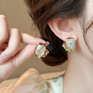 Close-up of baroque pearl earrings with colorful gemstones and golden floral accents