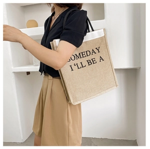 Side view of a natural linen tote bag with black handles and SOMEDAY printed text