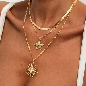 Dettaglio di una collana dorata a tre strati con ciondoli a forma di sole e stella marina