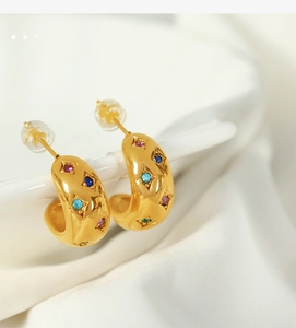 Close-up of golden C-shaped hoop earrings with colorful gemstones on white silk