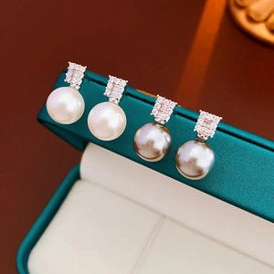 Macro shot of silver pearl stud earrings with sparkling cubic zirconia on green leather