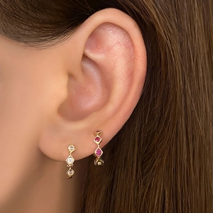 Close-up of golden hoop earrings with sparkling white and deep red zircon gemstones