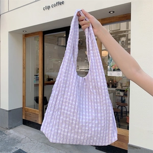 Detail of purple plaid canvas tote bag with textured fabric held by a model near a cafe