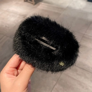 Detail of plush black faux fur hair clip with round golden metal logo ornament