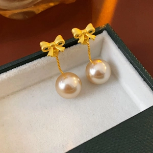 Macro detail of golden bow earrings with champagne pearls on a green velvet jewelry box