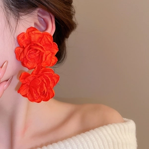 Macro shot of large vibrant orange-red silk rose earrings on model's ear with soft lighting