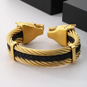 Macro detail of men's leather bracelet featuring a golden wolf head and steel cable braiding