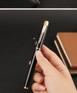 Close-up of black lacquered metal rollerball pen with gold arrow clip and leather notebook