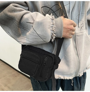Detail of a black denim crossbody bag featuring multiple zipper pockets and fabric texture