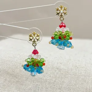Close-up of handmade beaded Christmas tree earrings with gold snowflake studs and colorful crystals