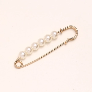 Detail view of a gold safety pin brooch with white pearls for waist adjustment