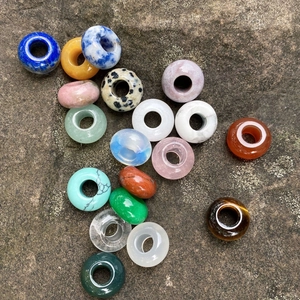 Various natural stone large hole rondelle beads on a grey rock surface for DIY jewelry